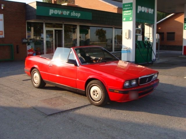 Un ancien cabriolet Maserati rouge devant le shop de la station