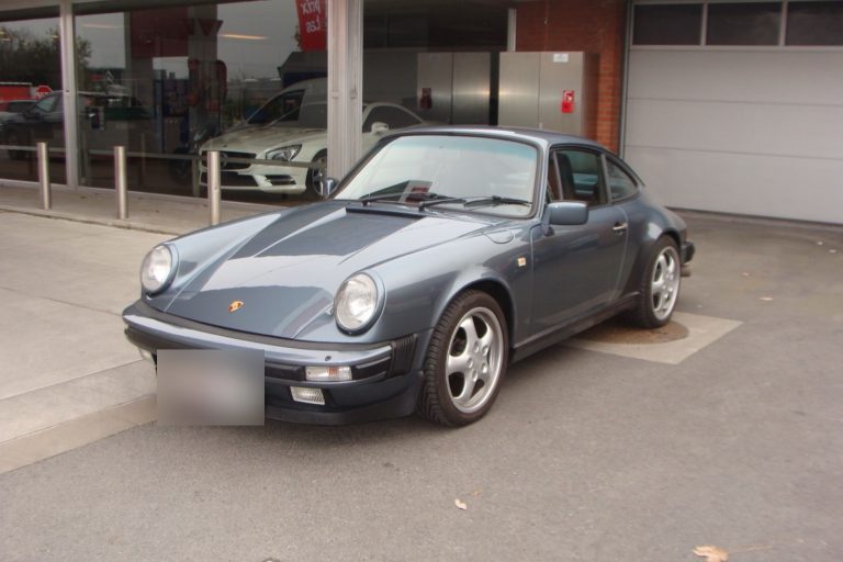 Une ancienne Porsche 911 grise sur la piste, devant le shop vitré de la station