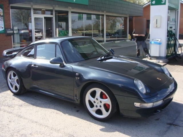Une Porsche 911 vert foncé devant le shop de la station