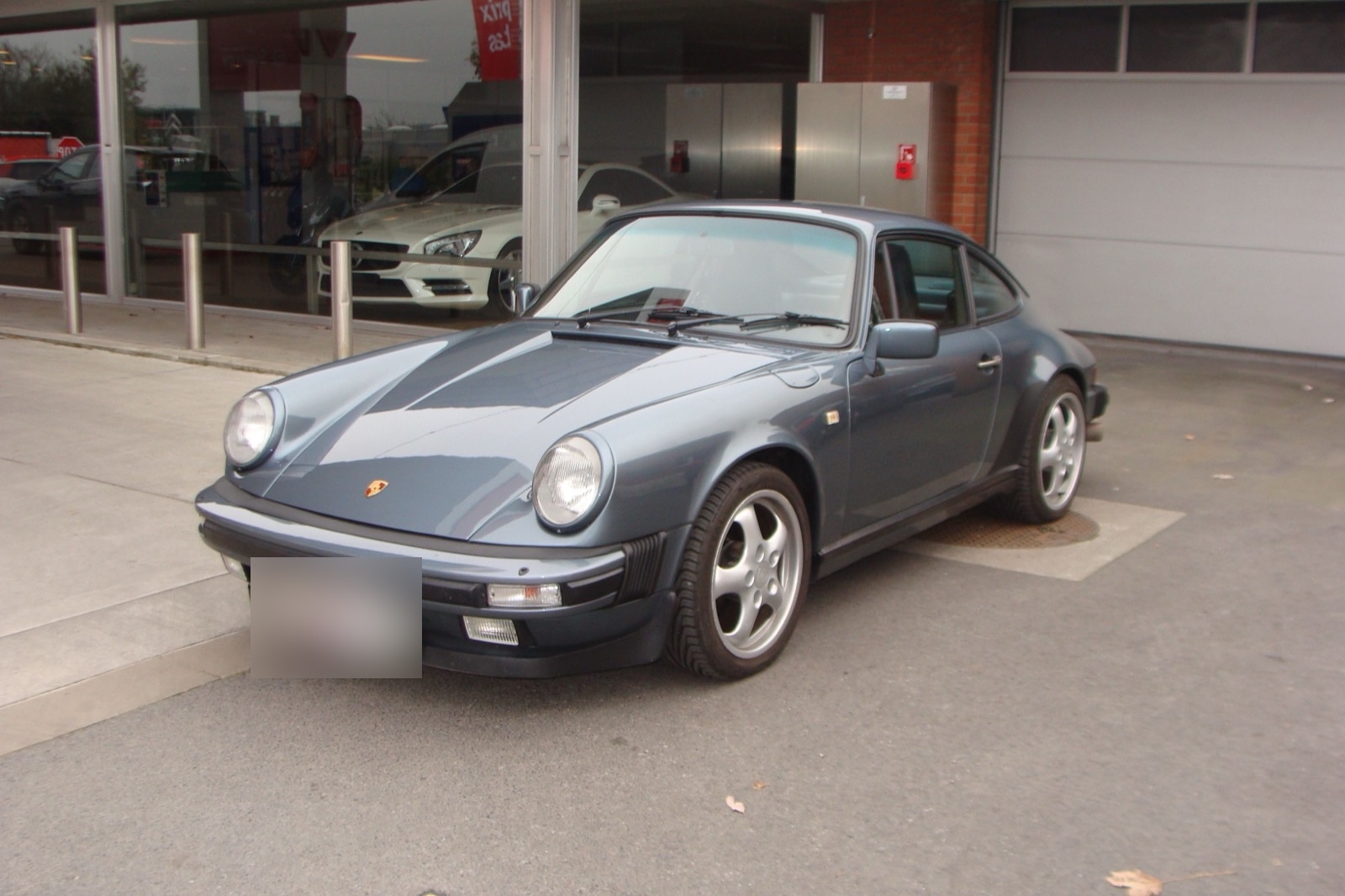 Une Porsche 911 grise sur la piste, devant le shop vitré de la station